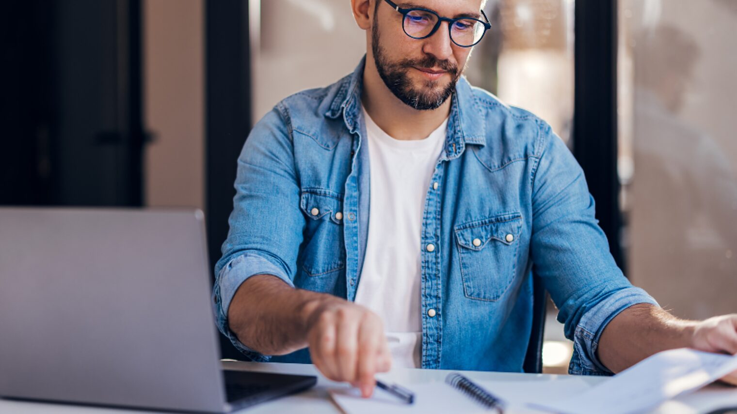 Mann mit Jeanshemd sitzt vor Computer.