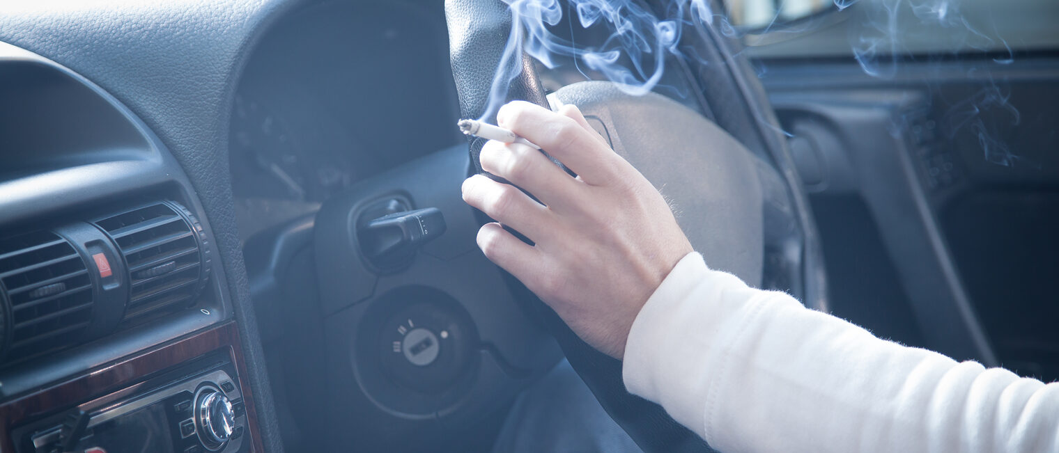 Person raucht Zigarette am Steuer eines Autos, Rauch füllt den Innenraum – Symbolbild für Rauchen und Luftverschmutzung.