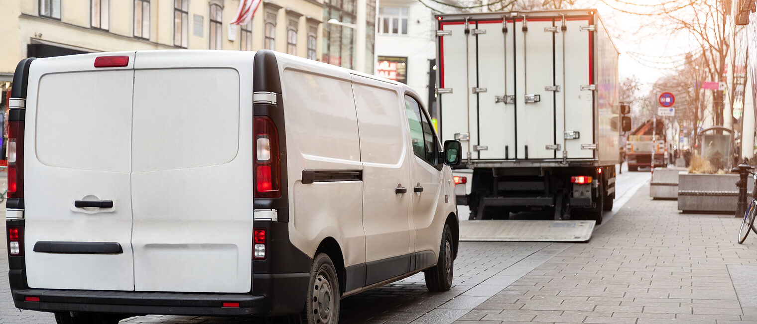 Lieferverkehr in der Innenstadt mit Transporter und Lkw Lieferwagen und Lkw beim Be- oder Entladen auf einer Innenstadtstraße mit Häuserfassaden und Pflastersteinen.
